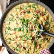 Top down view of creamy marry me butter beans in large shallow pan with black spatula.