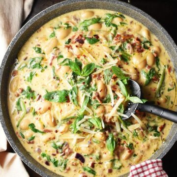 Top down view of creamy marry me butter beans in large shallow pan with black spatula.