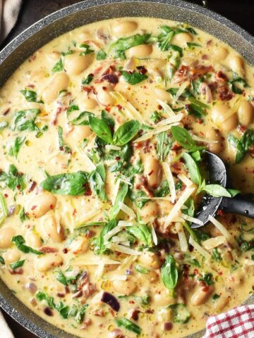 Top down view of creamy marry me butter beans in large shallow pan with black spatula.