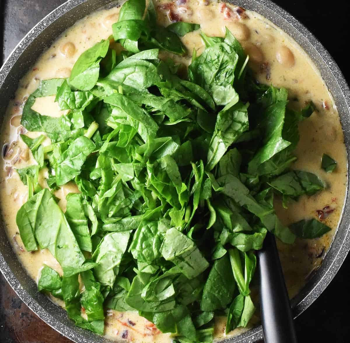 Chopped spinach in creamy sauce in large grey pan.