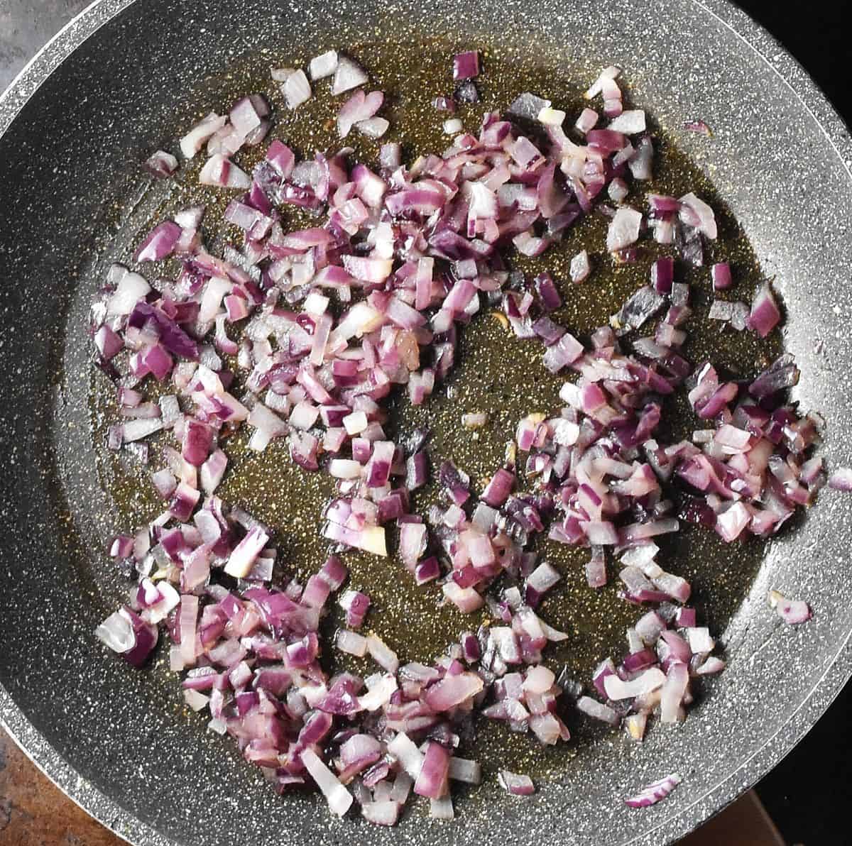 Top down view of chopped red onion in shallow speckled pan.