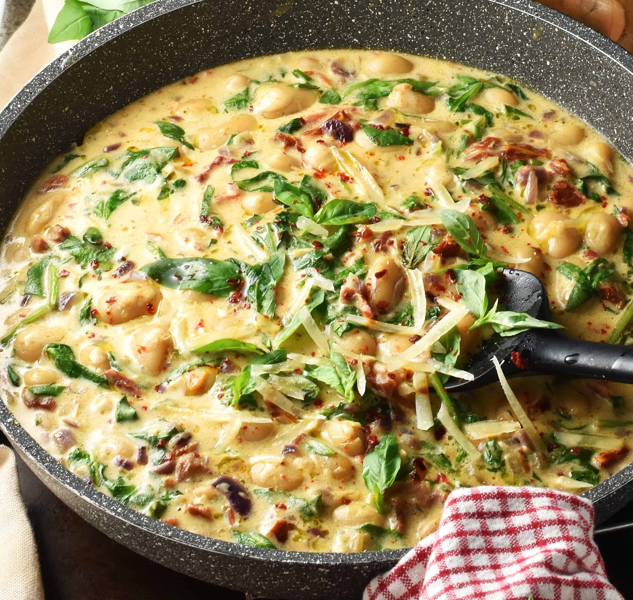Side view of butter beans in creamy sun-dried tomato sauce in large pan.