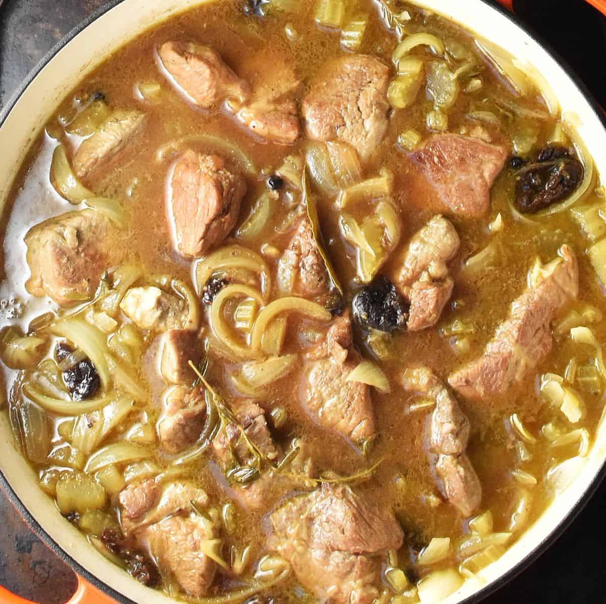 Top down view of pork pieces in broth with onion in white, shallow pan.