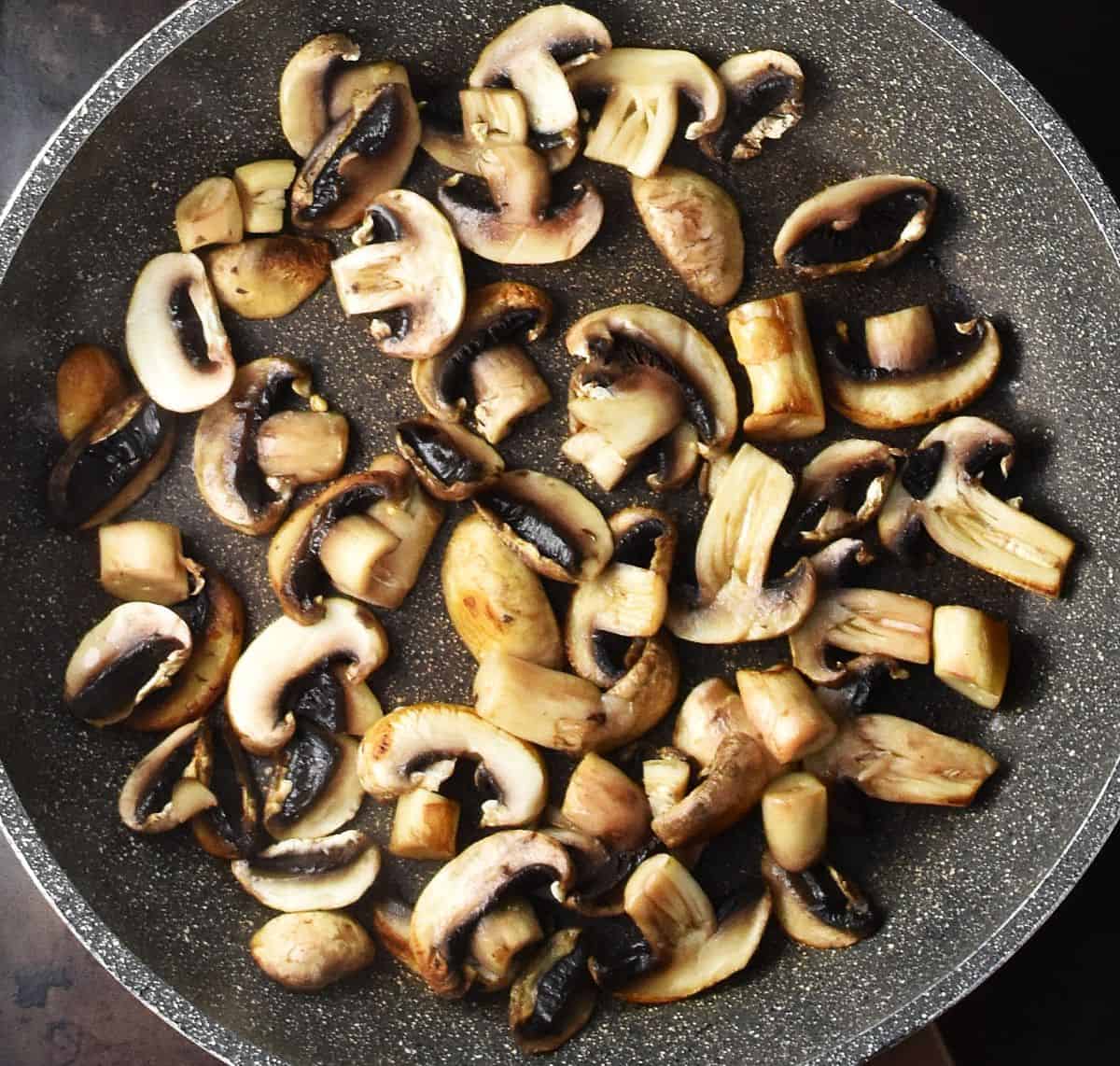 Top down view of sliced, browned mushrooms in large, grey pan.
