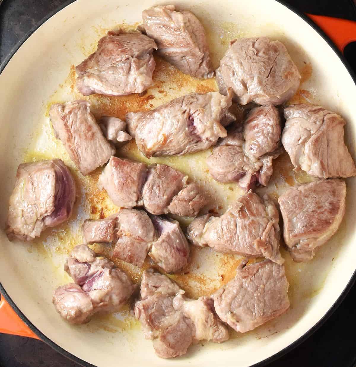Large pieces of pork shoulder searing in white, shallow pan.