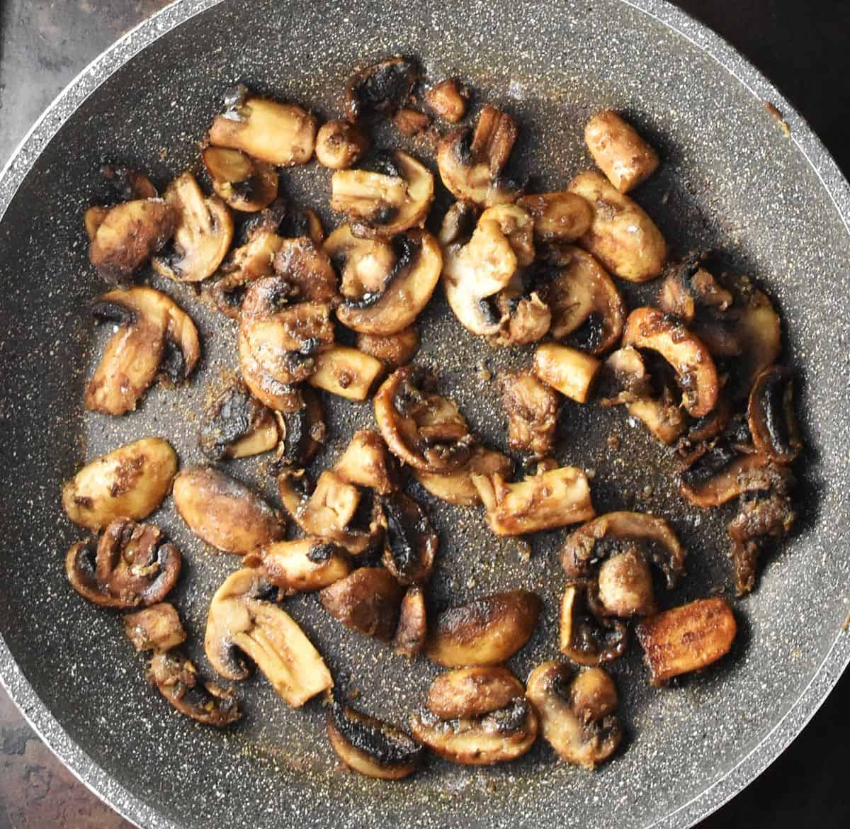 Top down view of browned sliced mushrooms in large pan.
