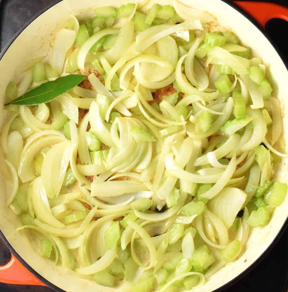 Sliced onion with bay leaf in large, shallow white pan.
