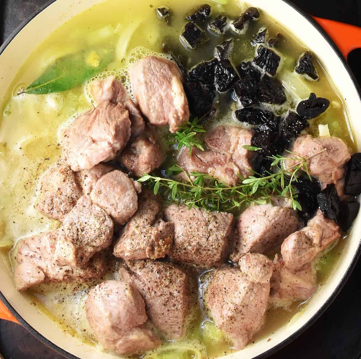 Large pieces of meat in broth with onion in large pan.