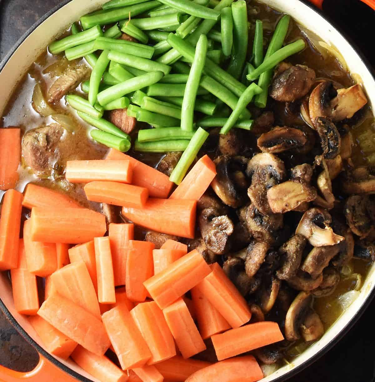 Stew with carrot pieces, green beans and sliced mushrooms on top in large pan.